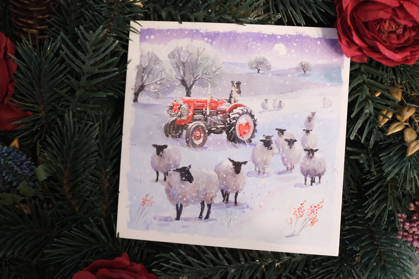 Christmas card with a tractor and sheep in a snowy landscape, surrounded by festive decorations.