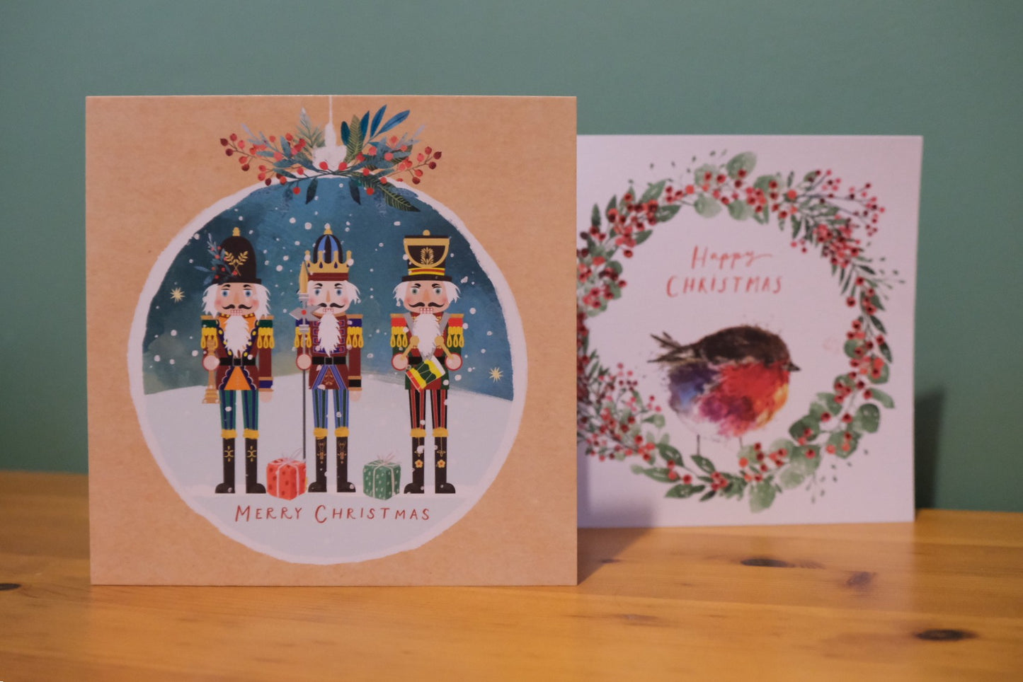 Two Christmas cards on a wooden surface with a green background