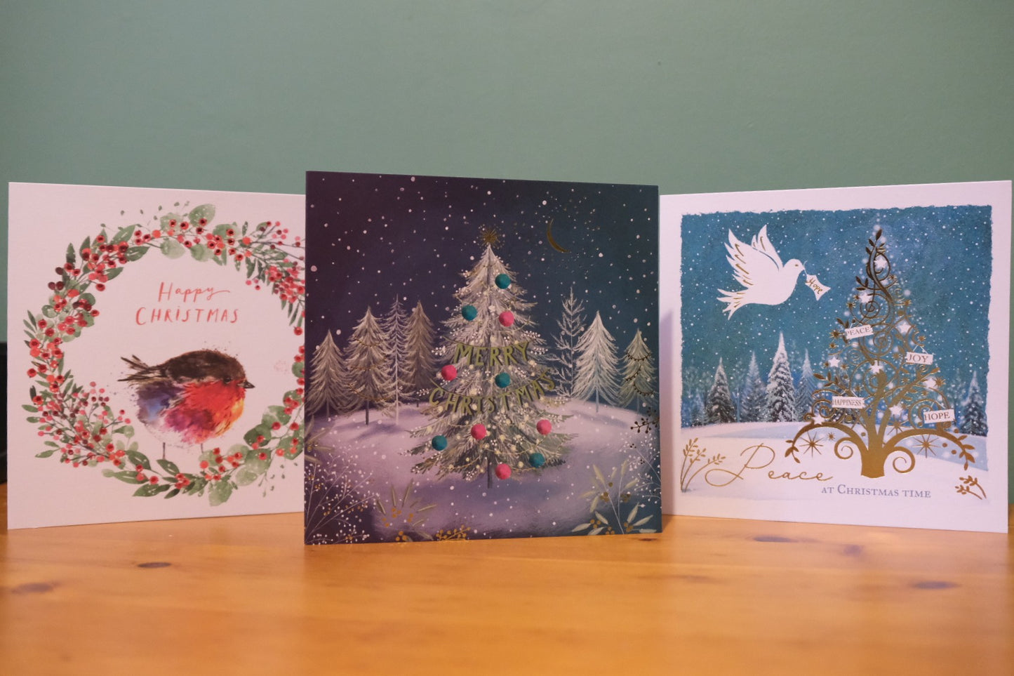 Three Christmas cards on a wooden surface with a green background