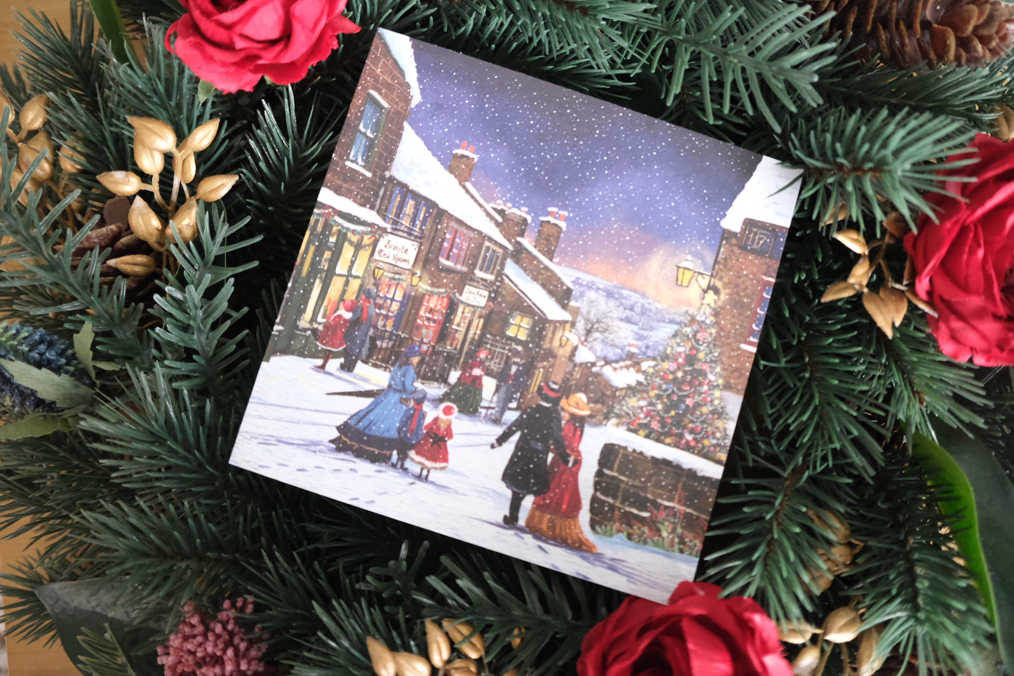 Christmas card depicting the village of Haworth, surrounded by festive greenery and red flowers.
