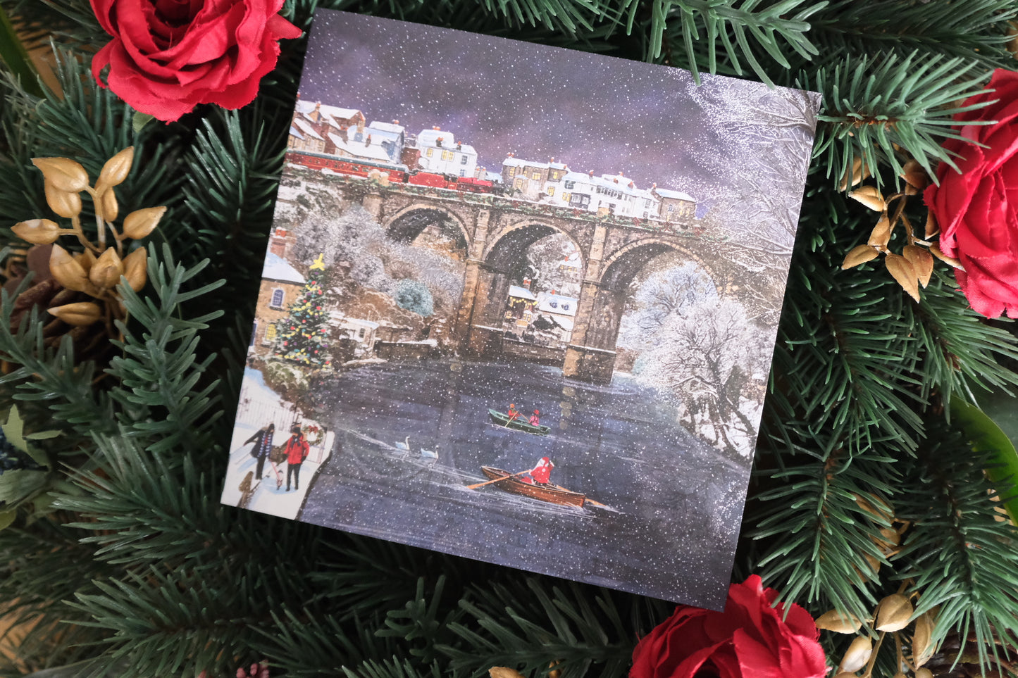 Card with a winter scene of the Knaresborough bridge and people on a snowy day, surrounded by Christmas decorations.