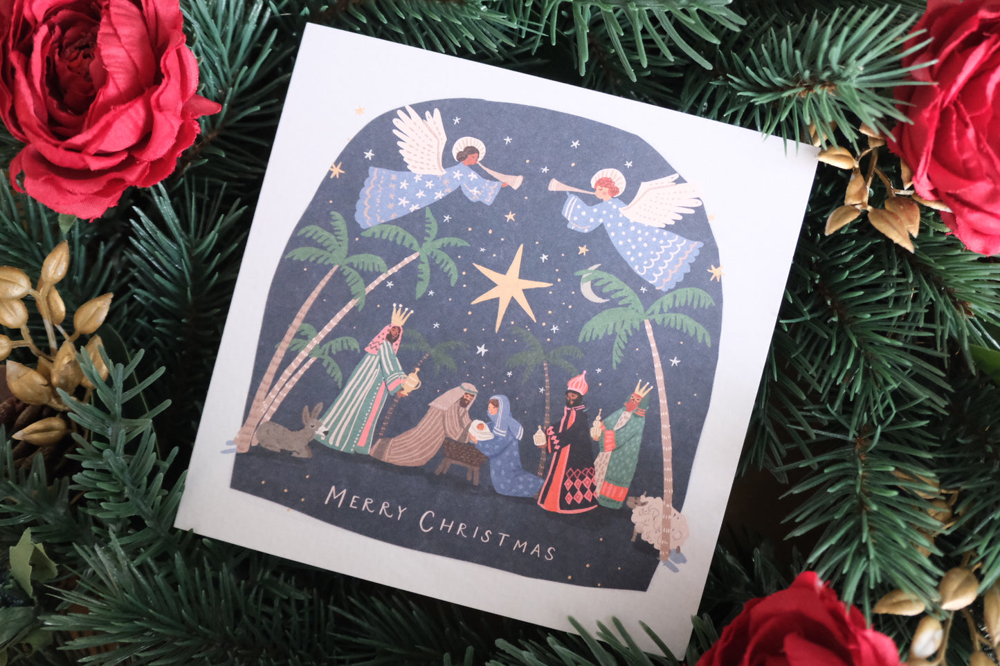 Christmas card with nativity scene surrounded by greenery and red roses