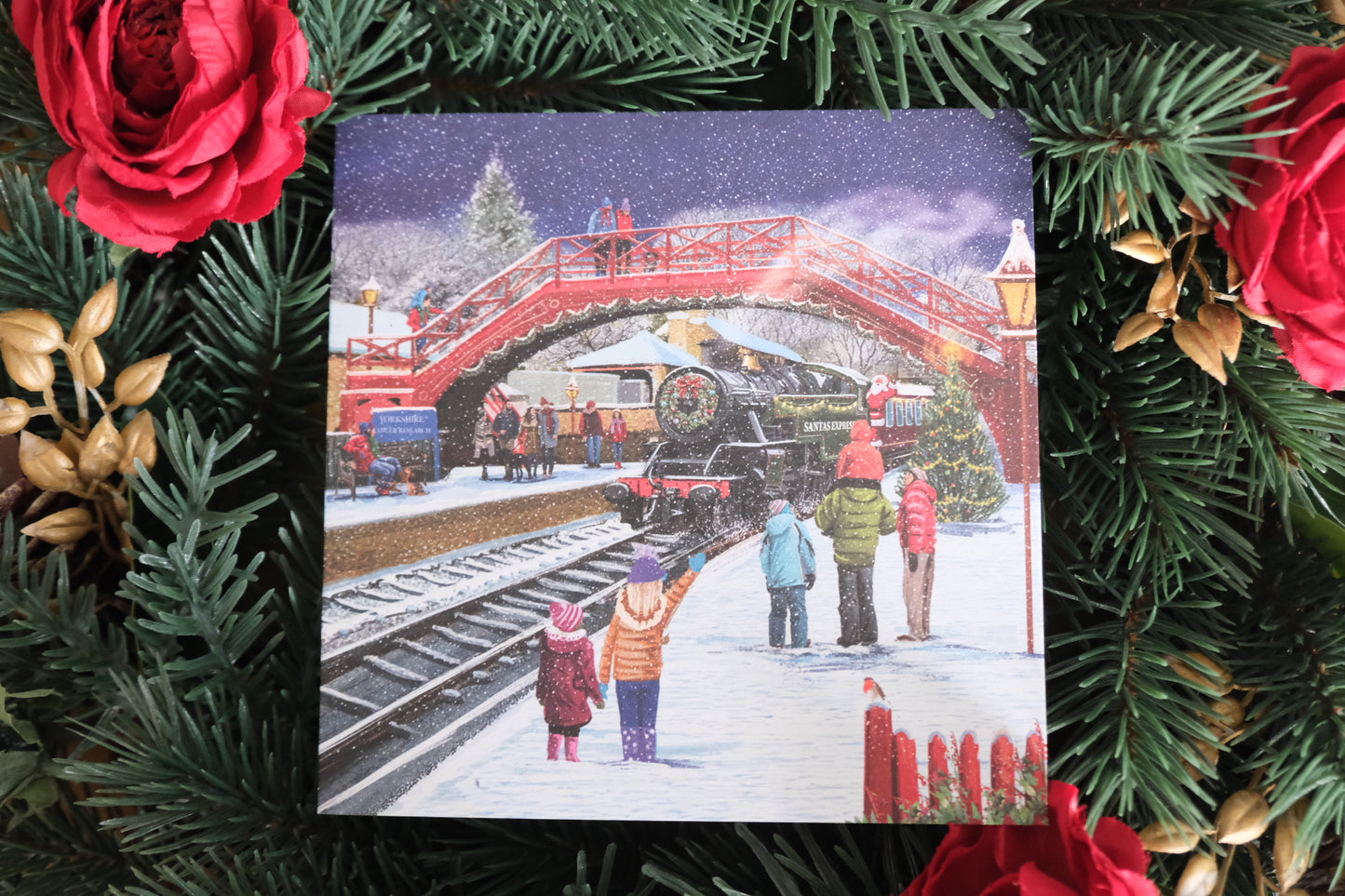 Christmas card with a snowy scene of people by a red bridge, surrounded by festive decorations.