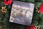 Card with a winter scene of the Knaresborough bridge and people on a snowy day, surrounded by Christmas decorations.
