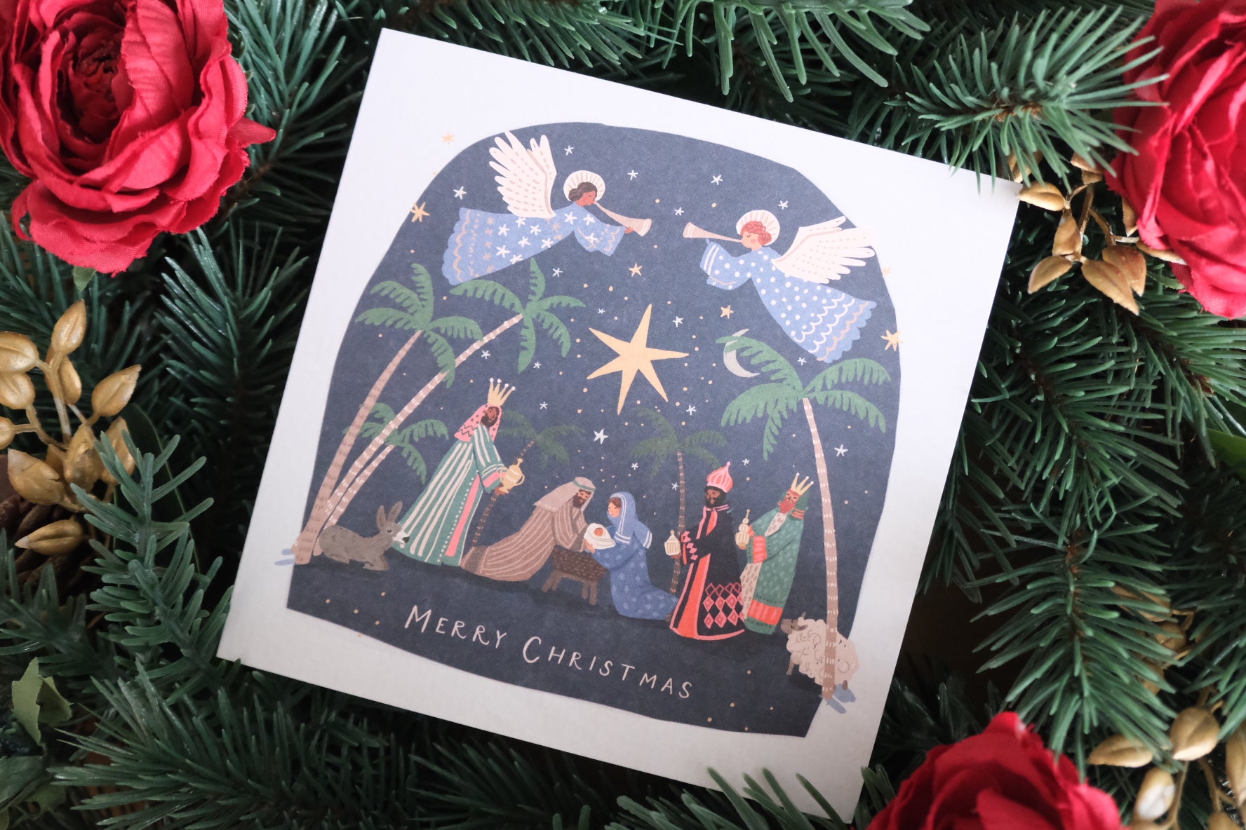 Christmas card with nativity scene surrounded by greenery and red roses