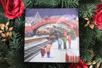 Christmas card with a snowy scene of people by a red bridge, surrounded by festive decorations.