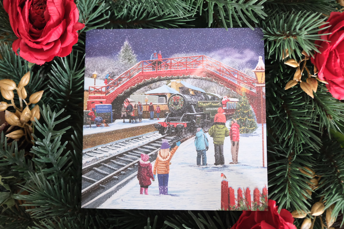 Christmas card with a snowy scene of people by a red bridge, surrounded by festive decorations.
